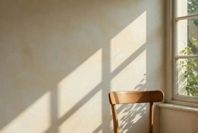 Sunlight across a pale wall, beside an empty timber chair and a window.